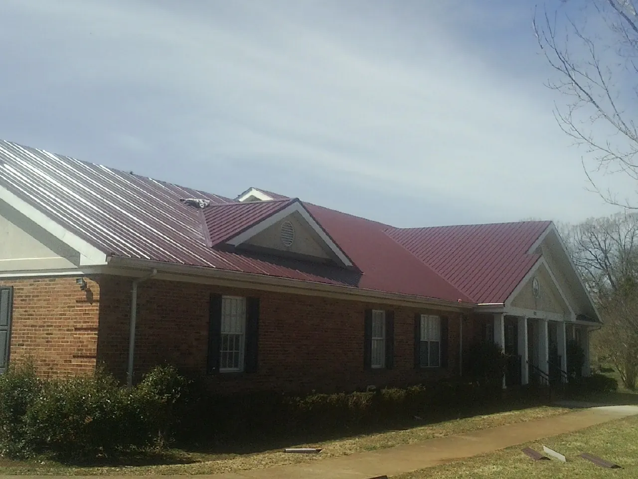 Red metal roof with gabled entries on a long brick building, from a Hail Damage Roof Repair job in Lava Hot Springs