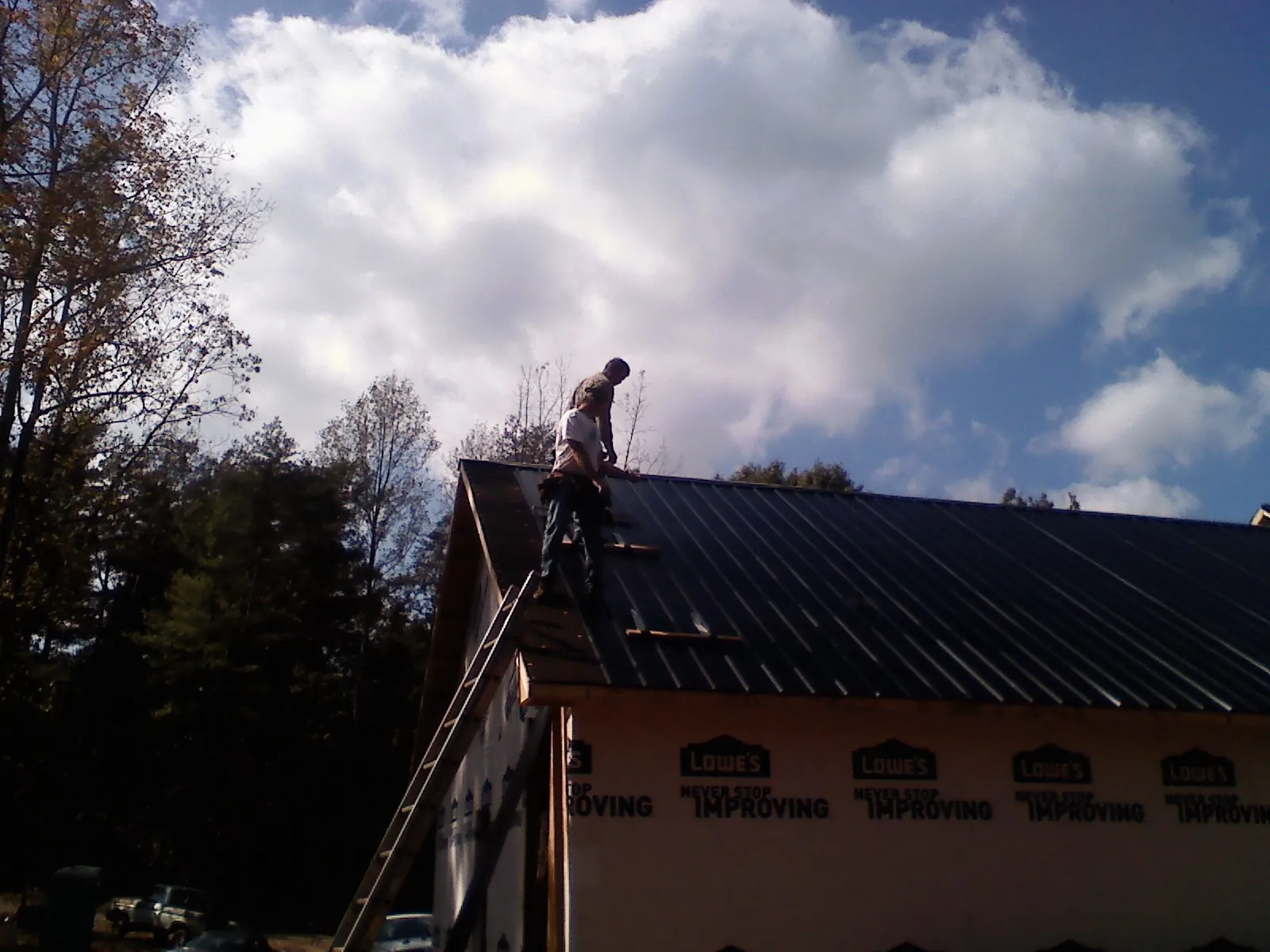Roofer fastening dark metal panels high against a cloudy sky, from a Roof Inspection job in Lava Hot Springs