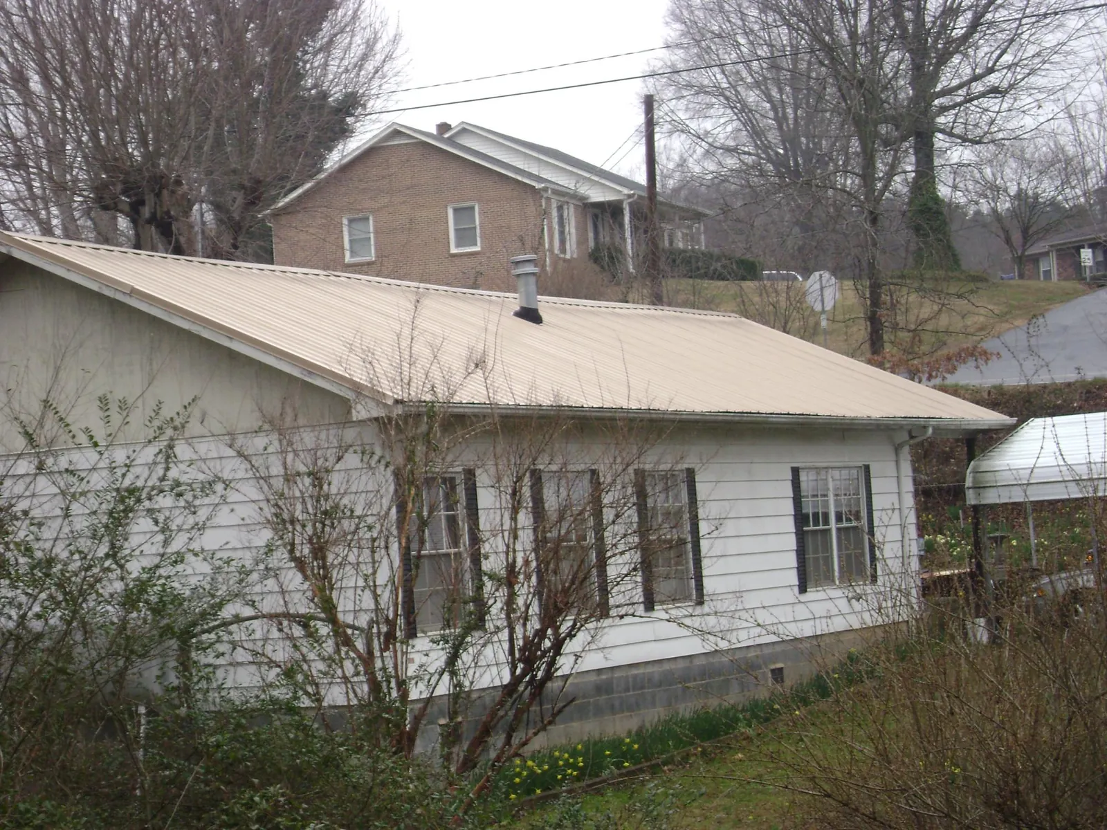 Tan metal roof on a white sided house set into a hillside — Commercial Roofing by Roofing Brothers in Lava Hot Springs